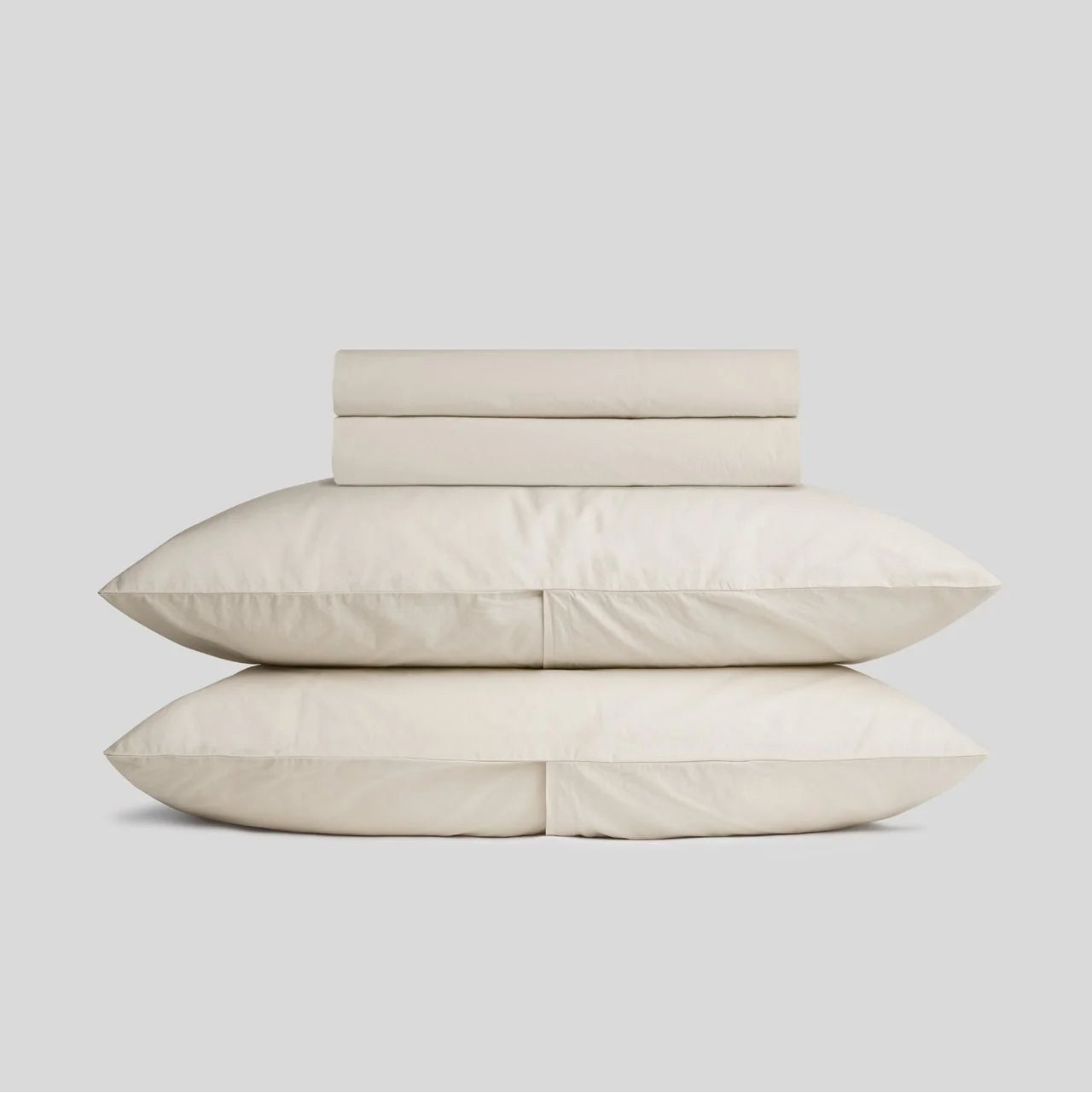 Light beige bed sheets and pillows stacked on a light gray background