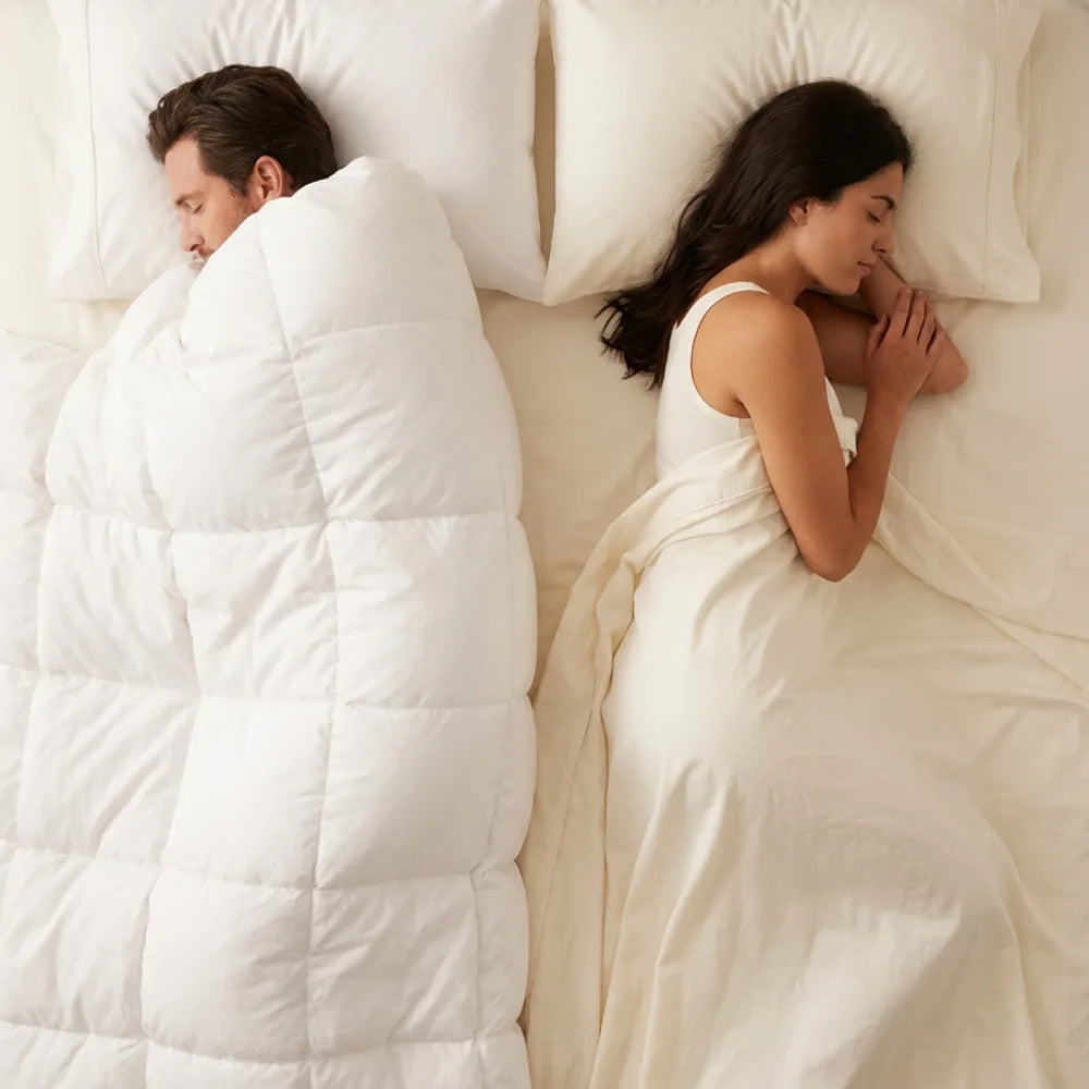 Aerial view of a couple in bed — one cocooned in a heavy duvet, the other uncovered