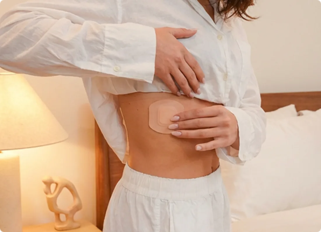 Woman applying an Orion sleep patch to her side in a softly lit bedroom.